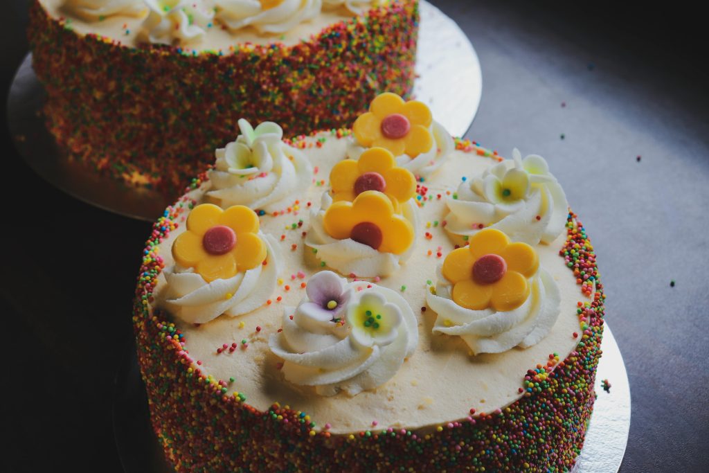 A close-up of a vibrant floral cake adorned with icing flowers and sprinkles, ideal for celebrations.